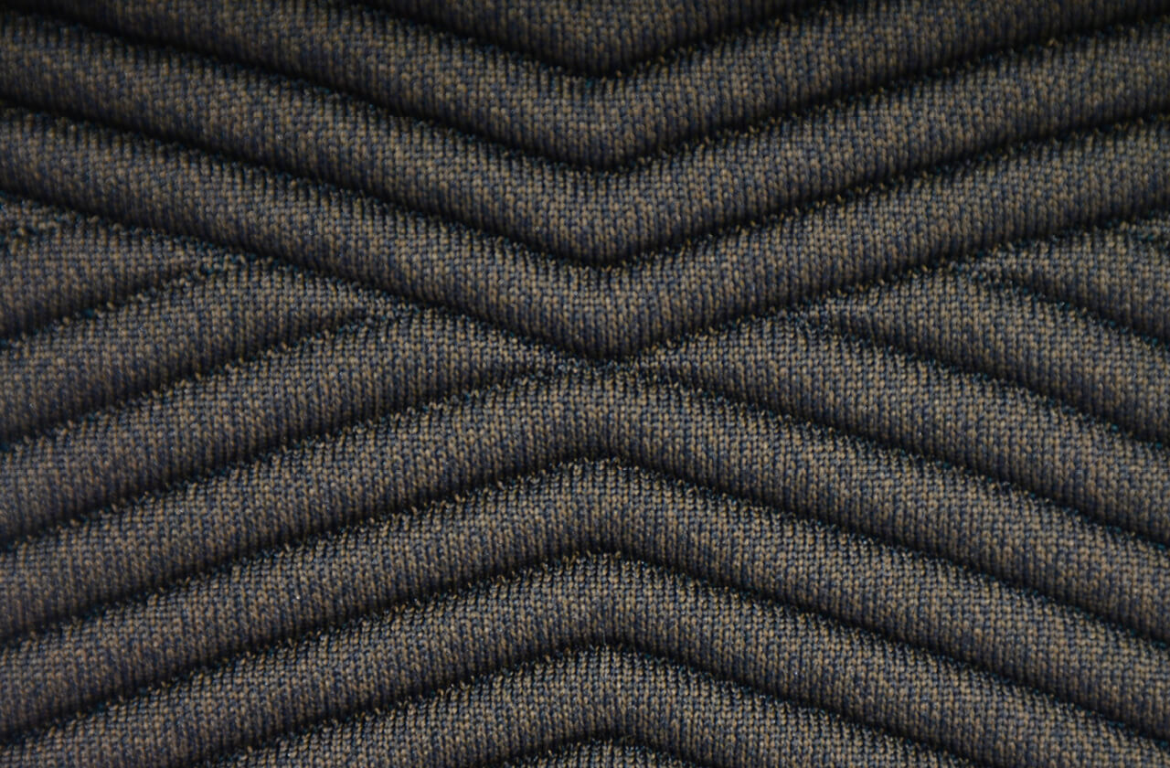 Nahaufnahme eines dunklen 3D-gestrickten Polsterbezugs im Fischgrätmuster – integriert, schaumfrei und nahtlos
